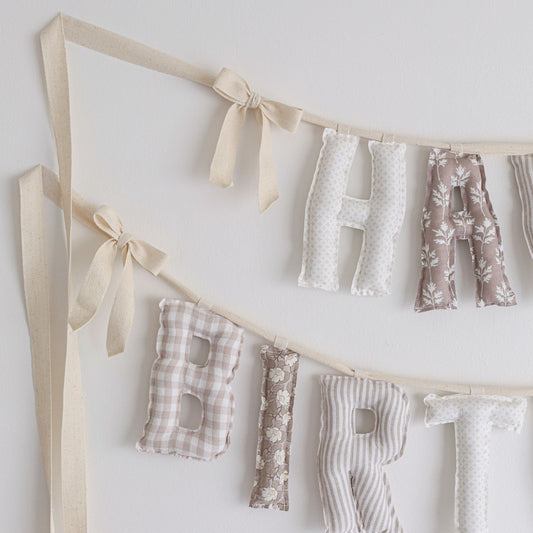 Close-up of Antique Birch birthday garland by Social Heirloom – soft cotton letters in cream, taupe, and brown gingham and floral prints, finished with natural twill bows for a classic heirloom look