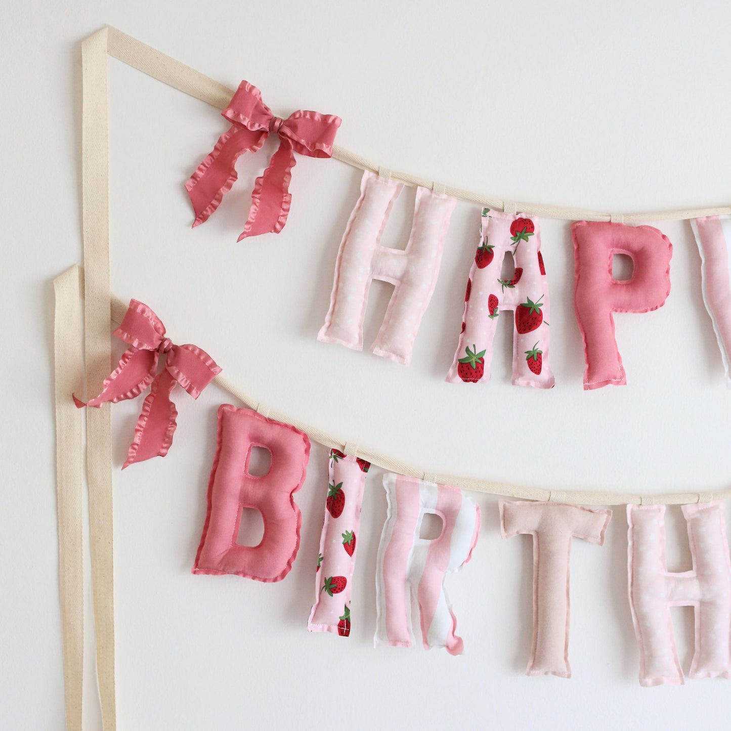 Close-up of Berry Sweet birthday garland by Social Heirloom – pink cotton letters with strawberry and dot prints, tied with pink ruffle bows, ideal for a berry-themed first birthday or sweet girl celebration