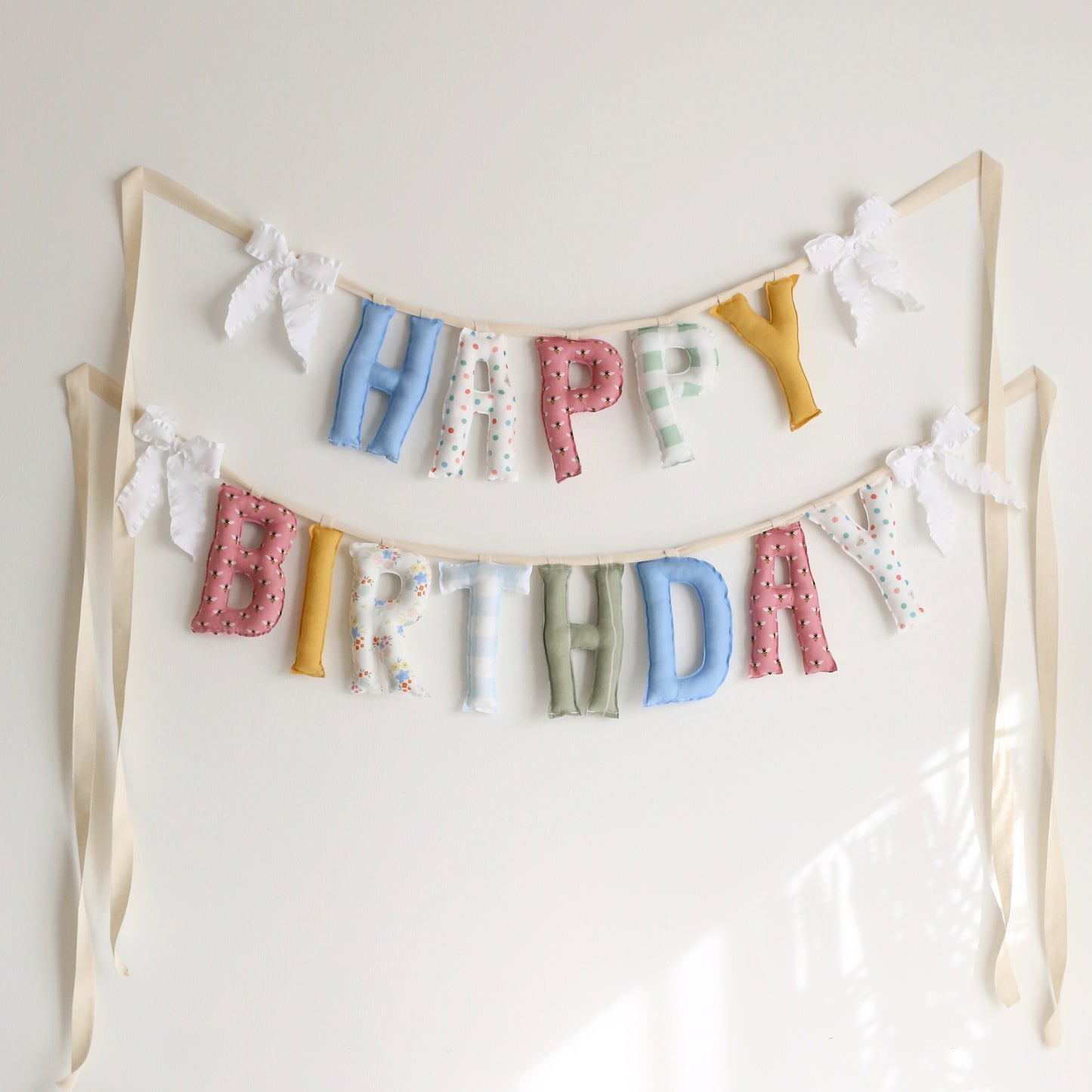 Big Day Parade handmade ‘Happy Birthday’ garland by Social Heirloom – playful mix of colorful florals, gingham, dots, and solids with white ruffle bows, perfect for first birthdays, playrooms, and joyful celebrations