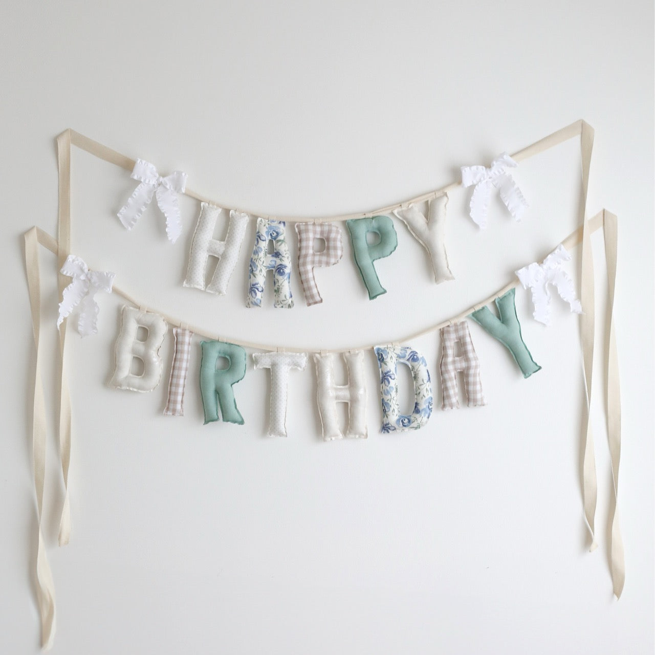 Handmade ‘Happy Birthday’ garland in Garden Window palette – soft green, blue, floral, gingham, and cream cotton letters with ruffle bows, perfect for first birthdays, nurseries, or heirloom celebrations by Social Heirloom
