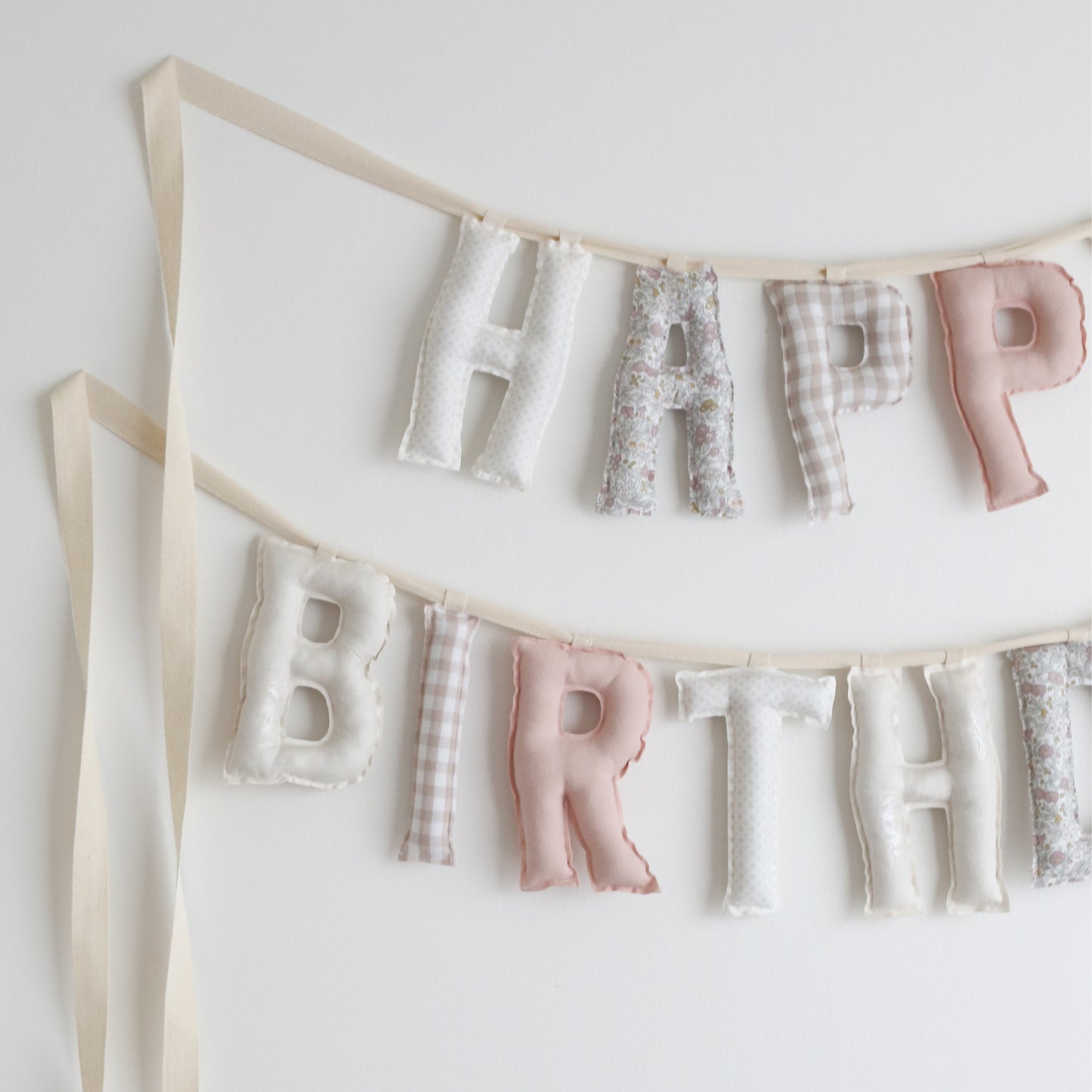 Close-up of handmade birthday garland in soft pink, cream, and floral fabrics – heirloom-quality cotton letters by Social Heirloom for nursery decor or first birthday celebrations