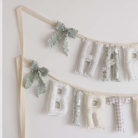 Close-up of handmade ‘Happy Birthday’ garland in Silly Goose palette by Social Heirloom – soft taupe, cream, gingham, floral, and goose print cotton letters with natural twill bows, perfect for a ‘One Silly Goose’ first birthday theme