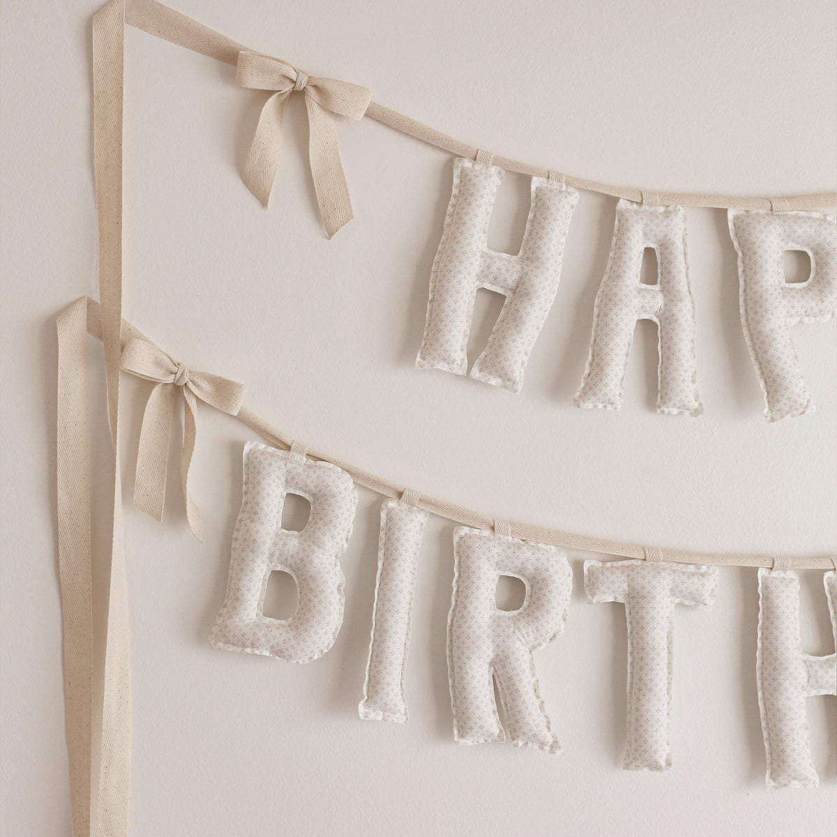 Close up of the Cotton & Cream Happy Birthday garland, soft filled fabric letters in soft creams, ivory and tiny pin dots