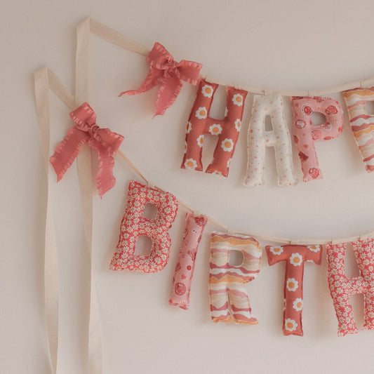 Close up of a Fabric Happy Birthday banner with pink 70s groovy print on a white wall