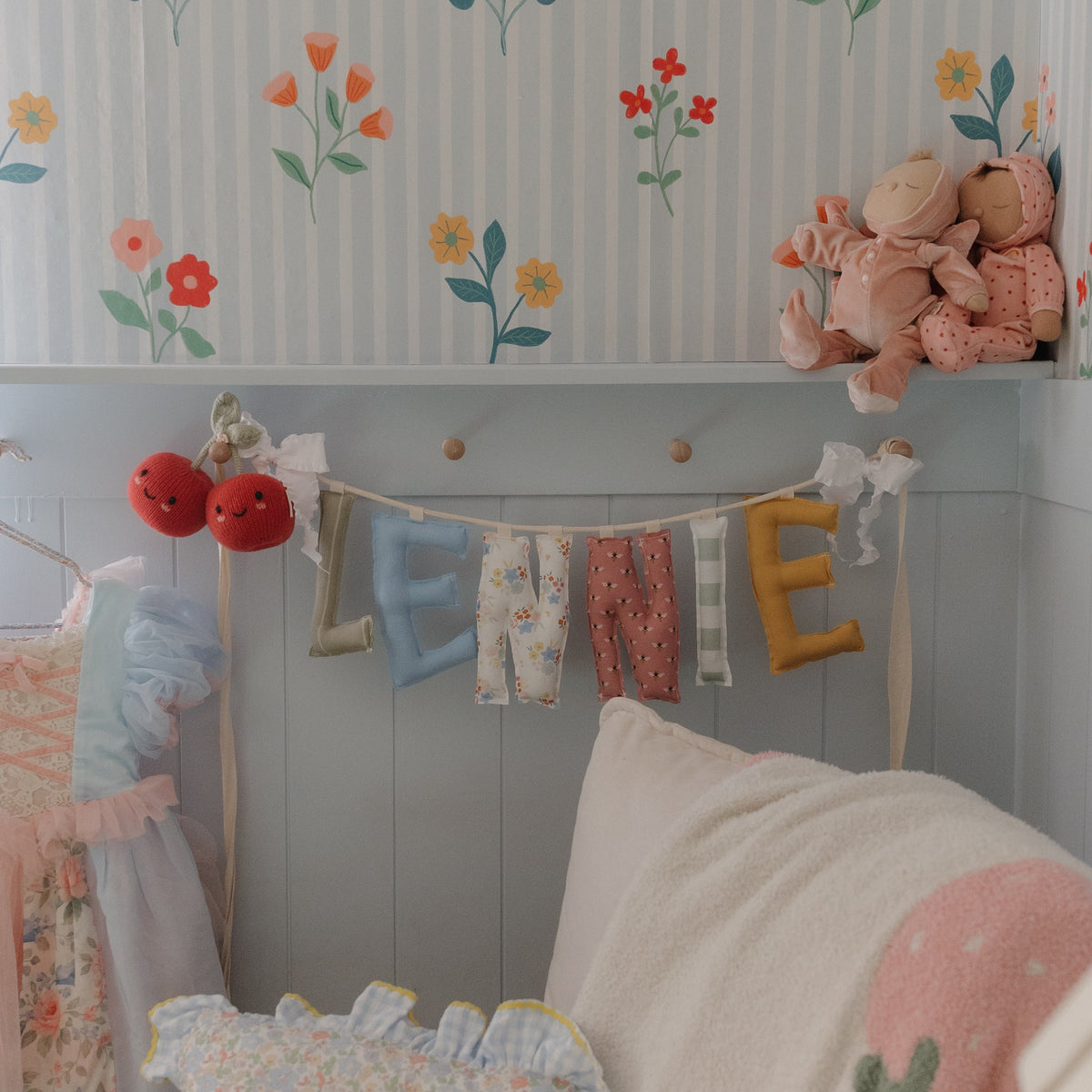 Big Day Parade personalized name garland spelling LENNIE hanging in a floral nursery, handmade fabric letters in colorful florals, mustard, berry dots, gingham and candy stripes by Social Heirloom