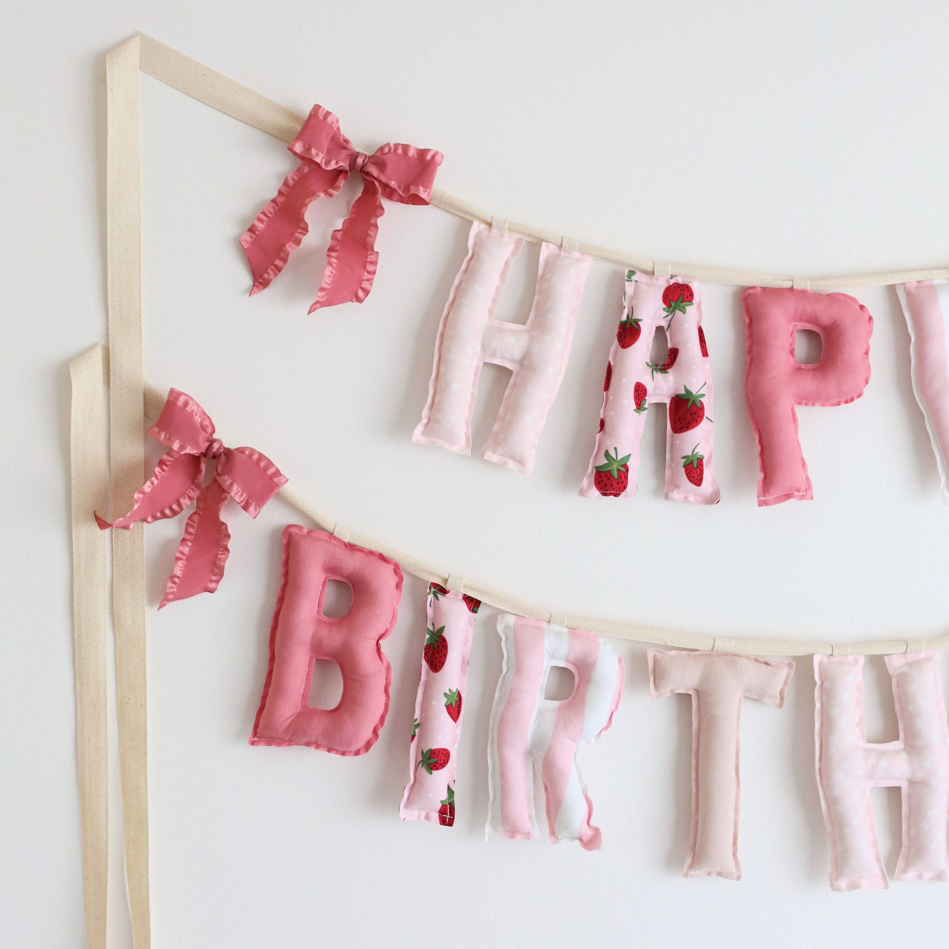 Close-up of Berry Sweet birthday garland by Social Heirloom – pink cotton letters with strawberry and dot prints, tied with pink ruffle bows, ideal for a berry-themed first birthday or sweet girl celebration