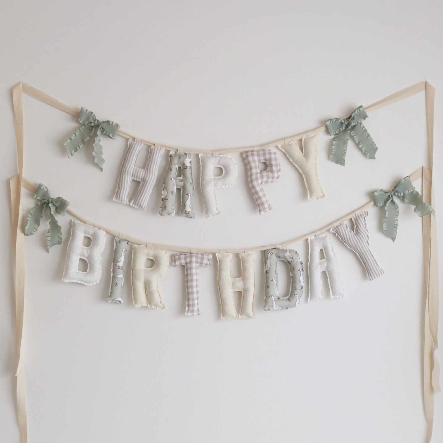 Handmade ‘Happy Birthday’ garland in soft neutral palette by Social Heirloom – features taupe gingham, floral prints, polka dots, and whimsical goose fabric, perfect for nurseries, baby birthdays, and a ‘One Silly Goose’ themed celebration