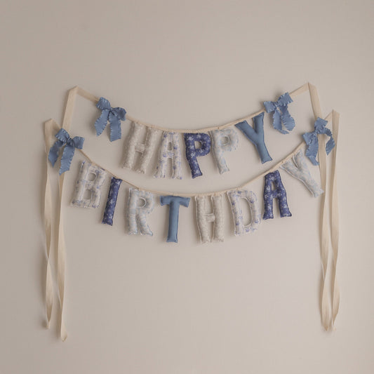 Decorative 'Happy Birthday' banner with blue and white elements on a plain wall.