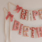 Close up of a Fabric Happy Birthday banner with pink 70s groovy print on a white wall