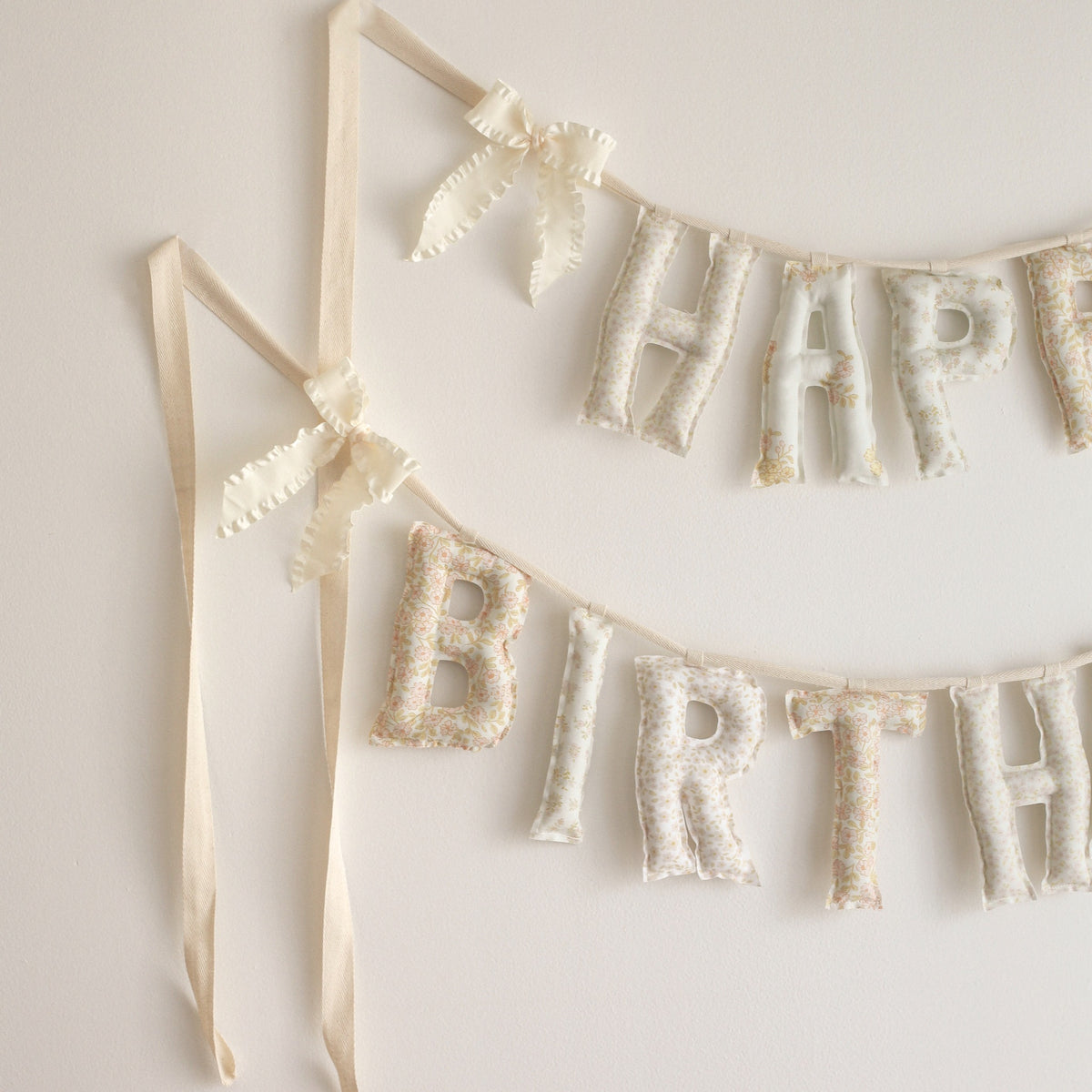 Close up of the Honey & Bloom Happy Birthday garland, soft filled fabric letters in pale vintage florals of blush, cream and buttery yellow