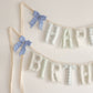 Close up of the Huckleberry Happy Birthday garland, soft filled fabric letters in soft blue stripes, sage gingham and sweet little checks in blue, green and oat