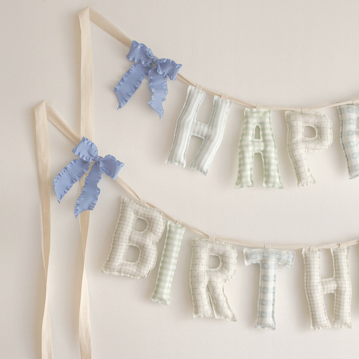 Close up of the Huckleberry Happy Birthday garland, soft filled fabric letters in soft blue stripes, sage gingham and sweet little checks in blue, green and oat