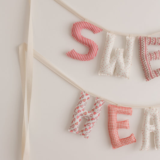 Fabric letter banner spelling 'SWEET HEART' on a white wall.