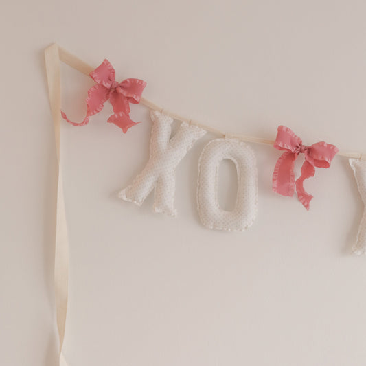 Decorative banner with 'XO' letters and pink bows on a light background