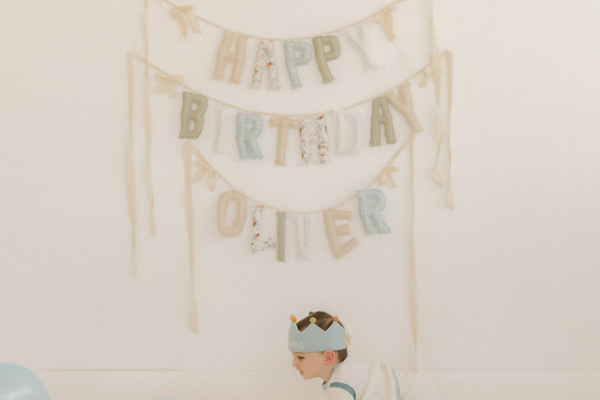 Child with balloons and a 'Happy Birthday Oliver' banner on a white wall