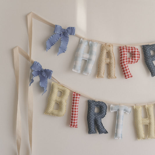 Decorative birthday banner with fabric letters spelling 'Happy Birthday' on a plain background.
