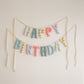 Wind-Up Circus Happy Birthday garland by Social Heirloom, handmade fabric letters in stars, harlequin diamonds, coral stripes and little blue flowers in teal, mustard, coral and pink