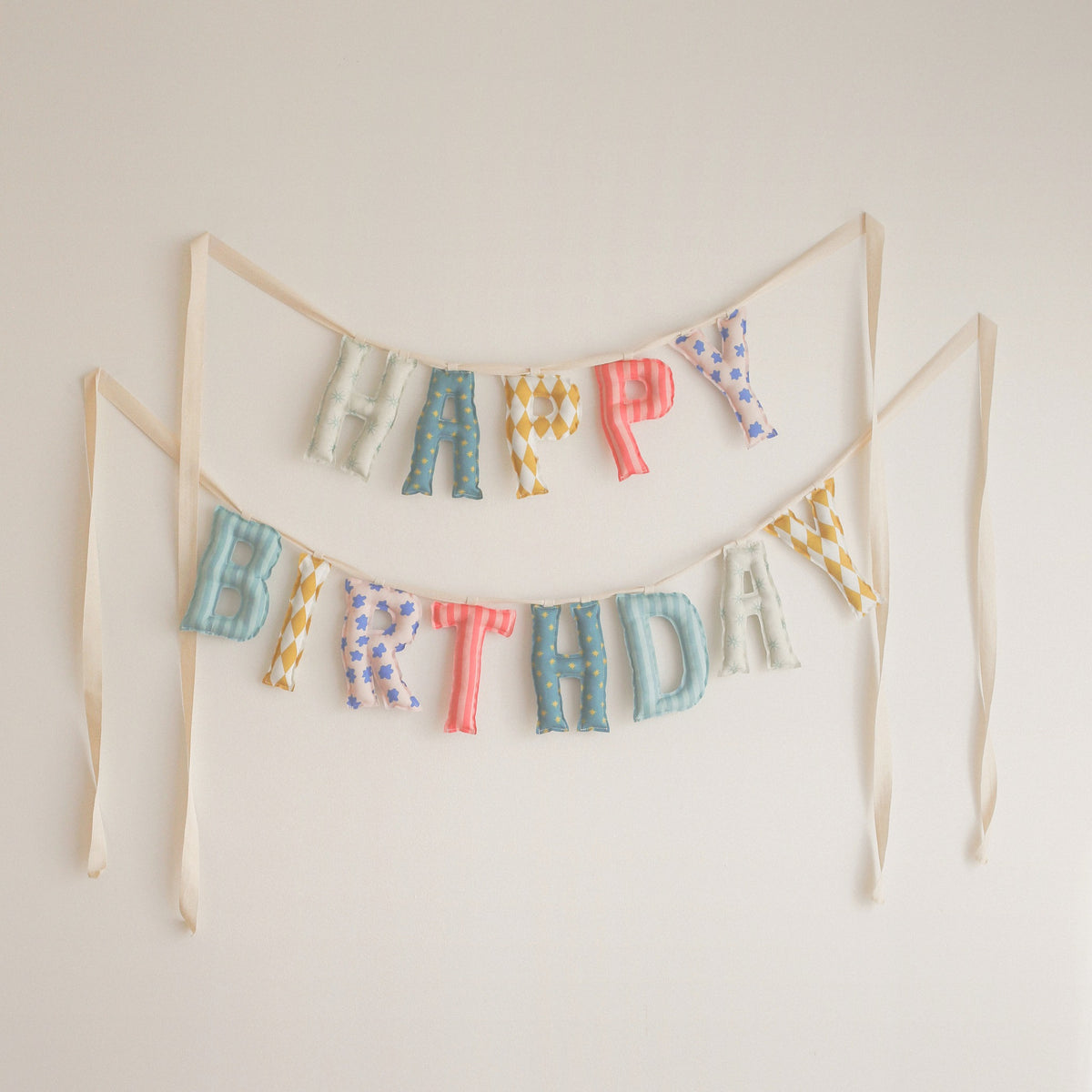 Wind-Up Circus Happy Birthday garland by Social Heirloom, handmade fabric letters in stars, harlequin diamonds, coral stripes and little blue flowers in teal, mustard, coral and pink